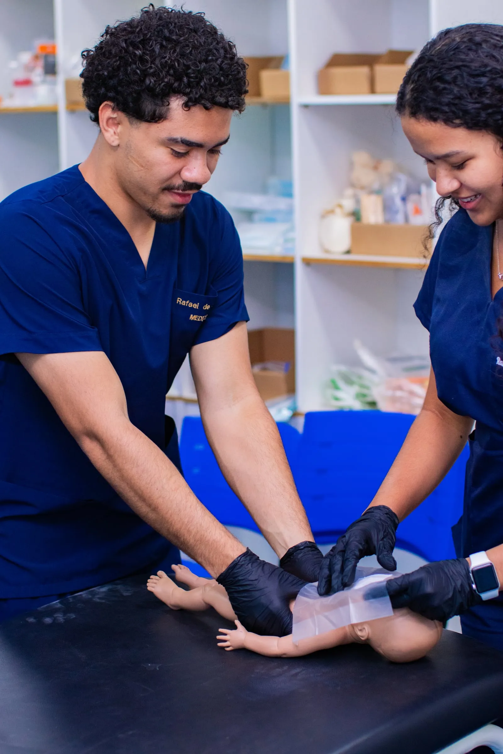 Dois estudantes de uniforme azul fazendo a manobra de reanimação em um manequim de recém-nascido