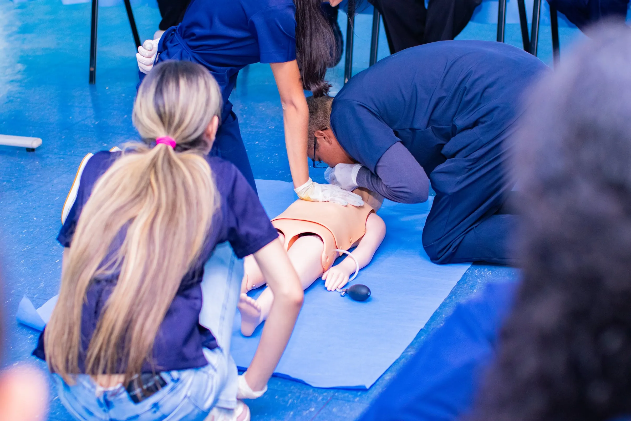 Dupla de estudantes praticando compressões em um manequim sobre o tatame